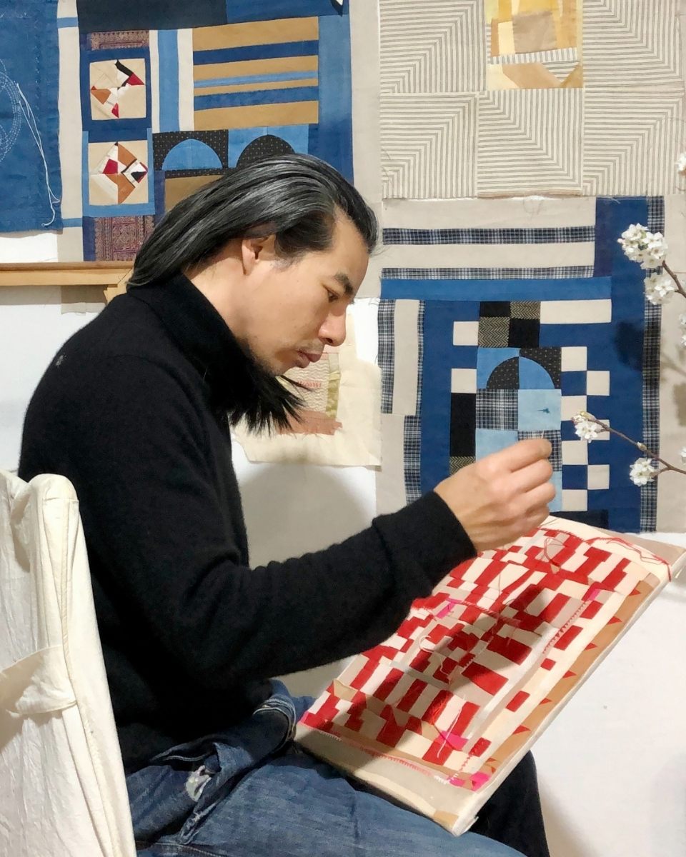 Side portrait of artist Phong Chi Lai focused on embroidering a contemporary textile piece in his studio.