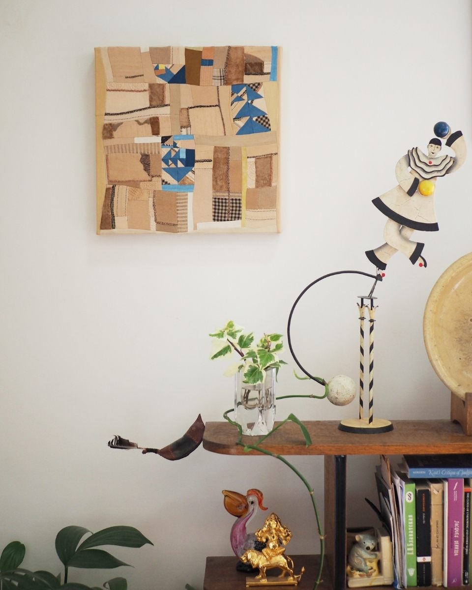 A minimalist artwork by Phong Chi Lai mounted on a wall, styled alongside a dark wood decorative shelf and sculptural home accents.