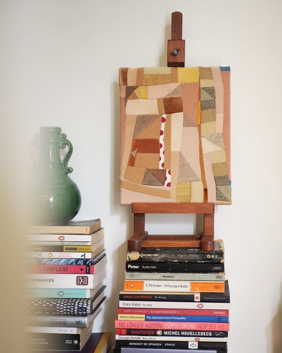 Phong Chi Lai’s mixed-media artwork displayed on a tabletop easel, elevated by a stack of art books in his intimate home studio.