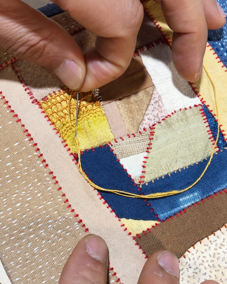 Macro close-up of Phong Chi Lai’s fingertips threading a needle through mixed media artwork, highlighting the precision of his embroidered art.