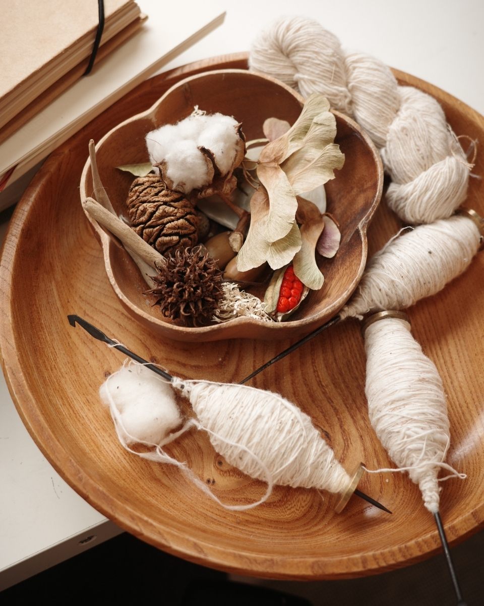 Detail of a wooden plate in Rachna Garodia’s London studio, holding a curation of cotton loom threads, raw cotton blossoms, and foraged natural elements.