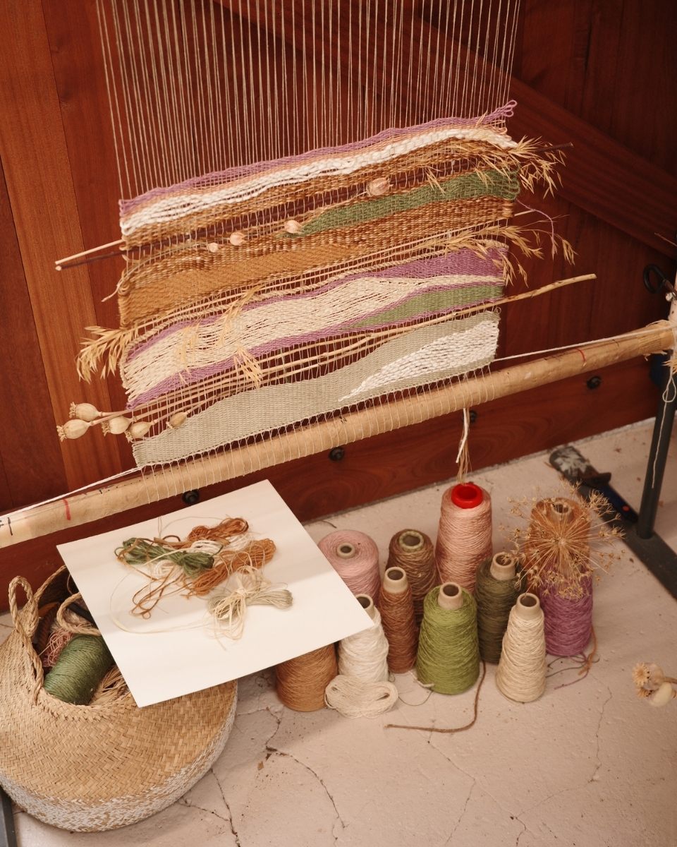 Rachna Garodia’s textile artwork in progress on a loom, showing the rhythmic interlacing of natural yarns with foraged organic materials.