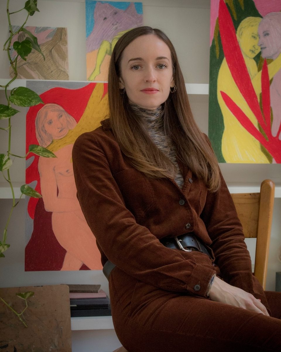 Seated portrait of artist Rebecca Sammon in her studio in front of her oil pastel artworks.
