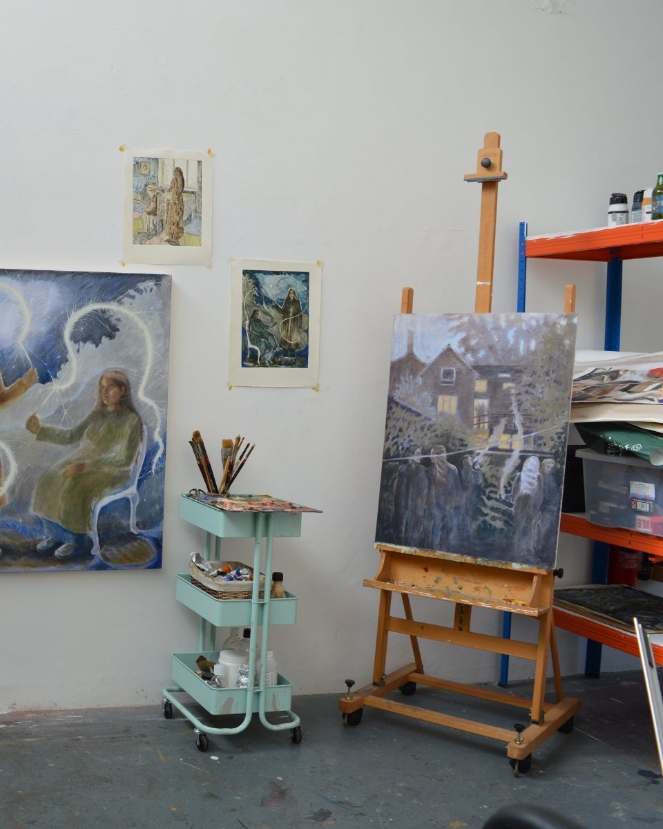 Studio view of Robyn Packham’s workspace, depicting an organised art tool trolley, works on an easel, and paintings.