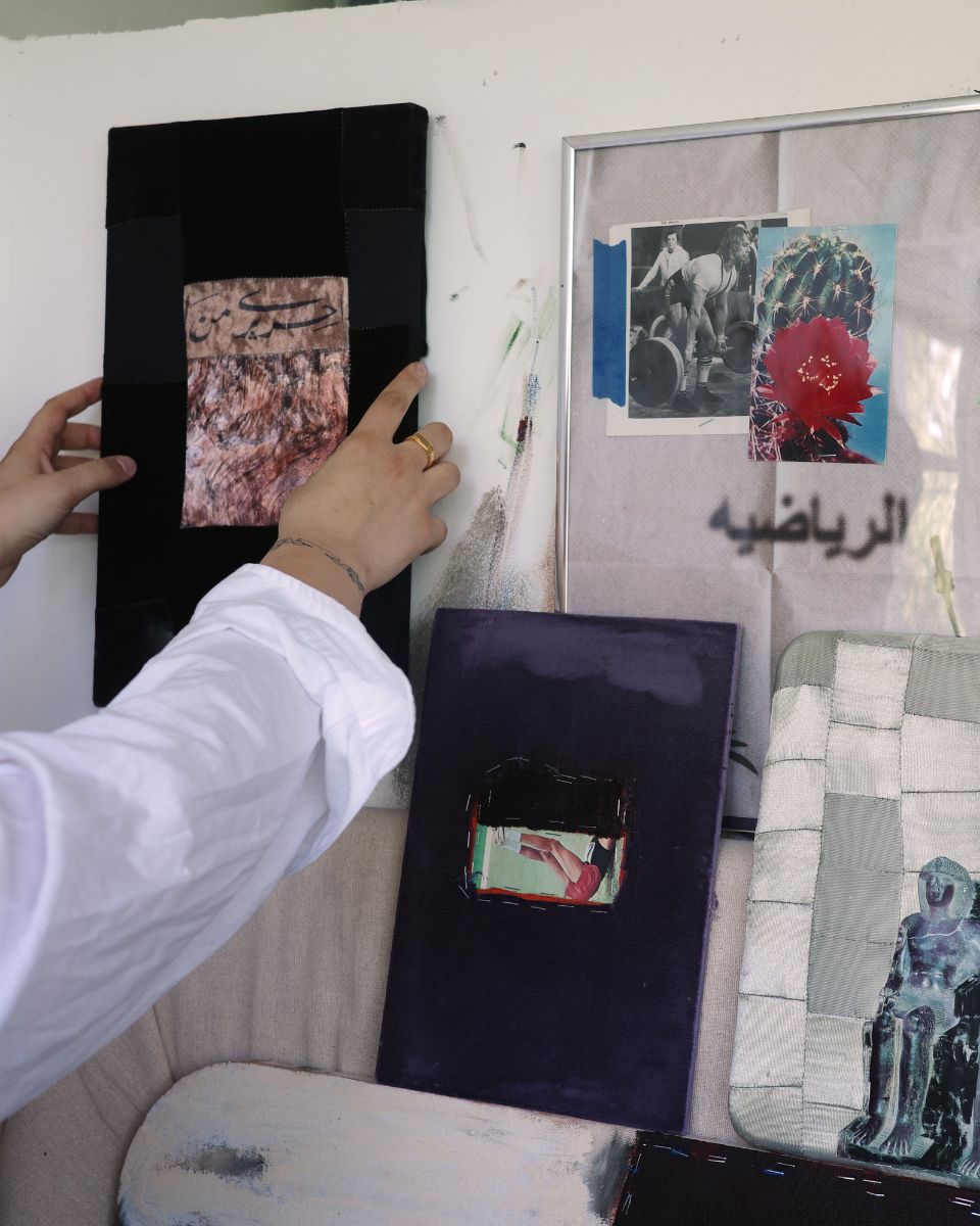 Ruba Nadar mounting a small-scale abstract painting onto her studio wall next to other artwork.