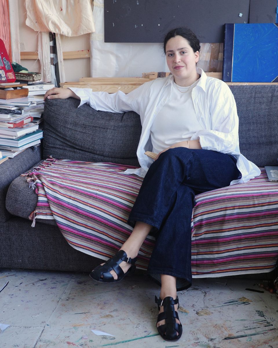 A relaxed environmental portrait of artist Ruba Nadar seated on a cozy sofa inside her creative studio.