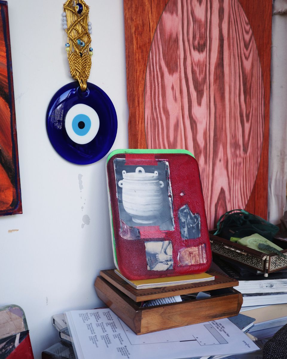 Detail of an evil eye talisman hanging next to sketches, books, and notes on Ruba Nadar's studio wall.