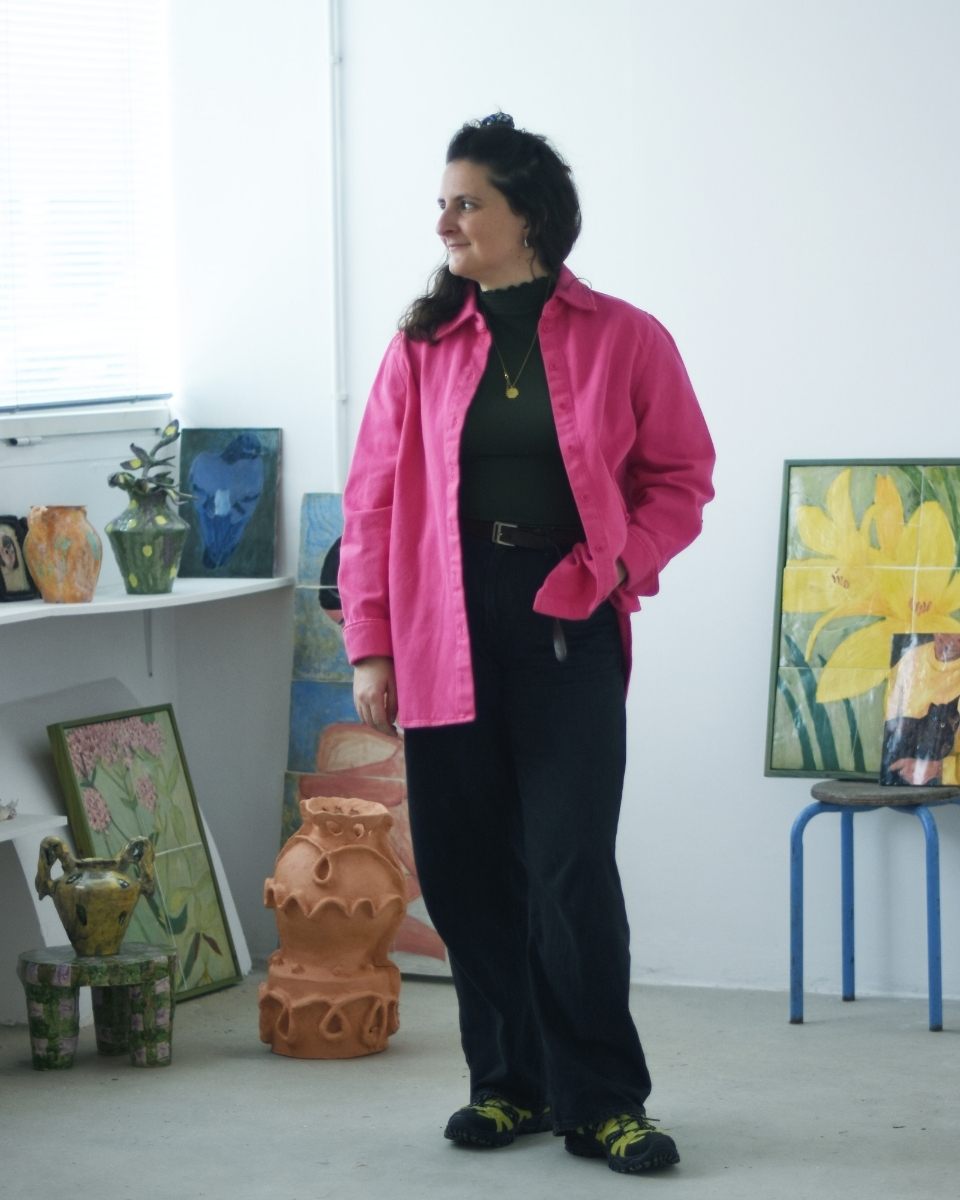 Full-length portrait of a smiling Samantha Kerdine in her studio with her paintings and sculptural ceramics.