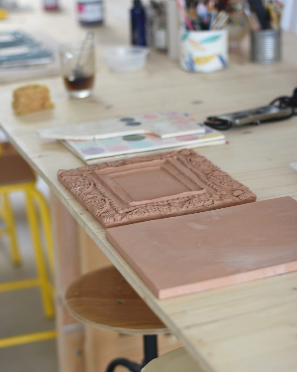 A detail shot of Samantha Kerdine’s studio featuring raw, hand-sculpted clay frames ready for underglaze painting and firing.