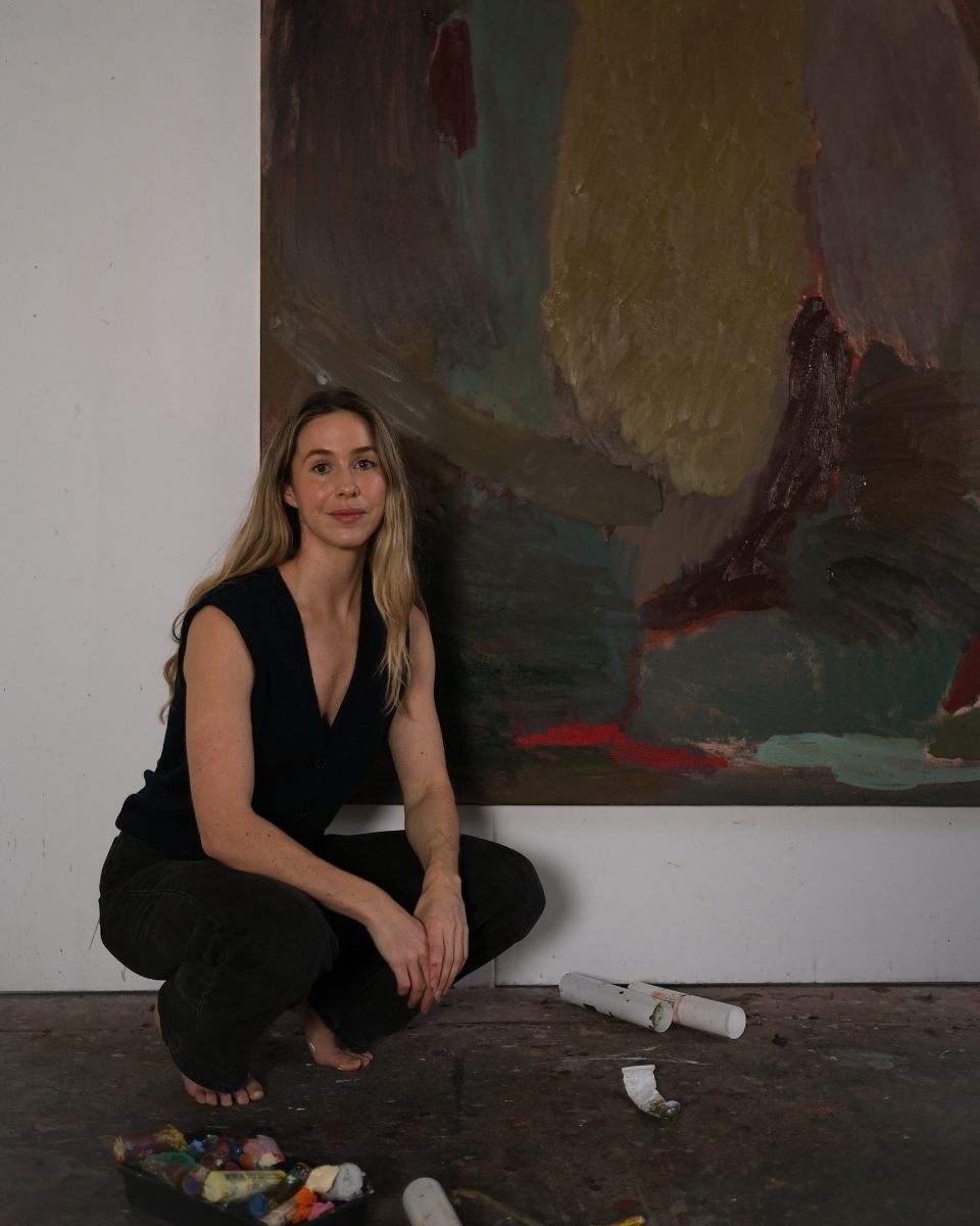 Artist Sara Winfield crouched in her studio in front of her monumental abstract painting 'Night Feed 03,' emphasising the scale of her work.