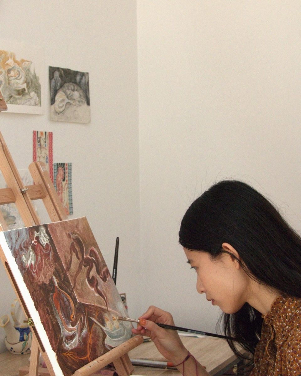 Shaoyu Chen in her studio, carefully adding finishing touches to a symbolic abstract painting on a tabletop easel.