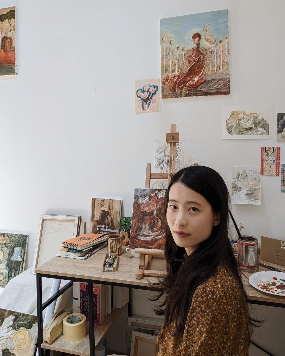 A serene portrait of artist Shaoyu Chen seated at her studio desk, surrounded by the tools and inspirations for her collections.