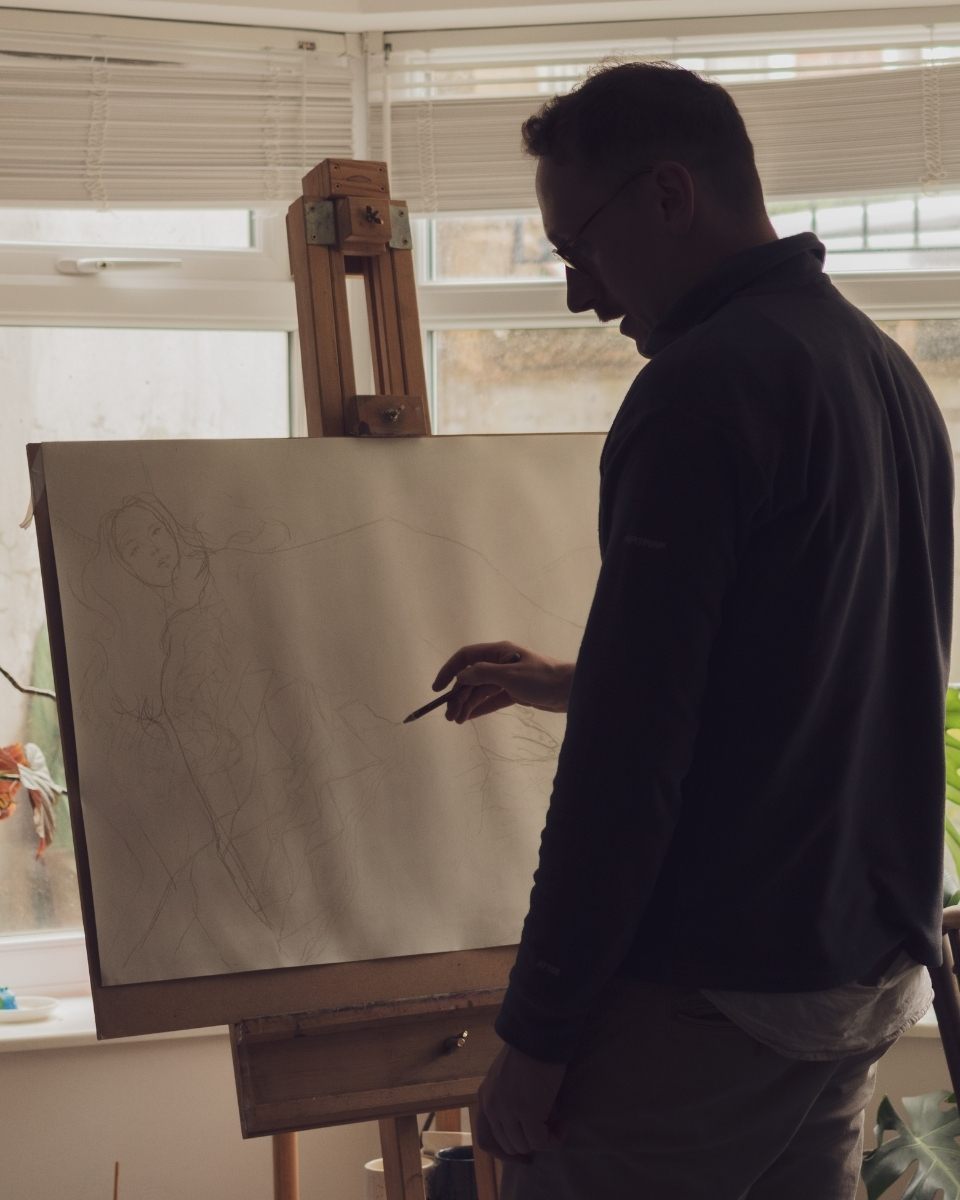 Artist Shaun Duke in his London studio, carefully outlining a central figure on an easel for a new narrative-driven composition.