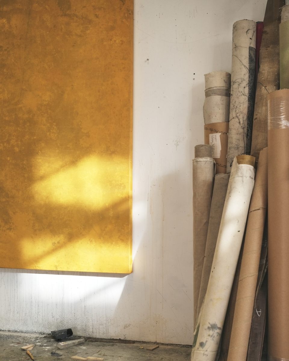 A sneak peek into Simon Job’s London studio, showing the corner of a textured abstract painting and a series of rolled-up heavy-duty canvases.