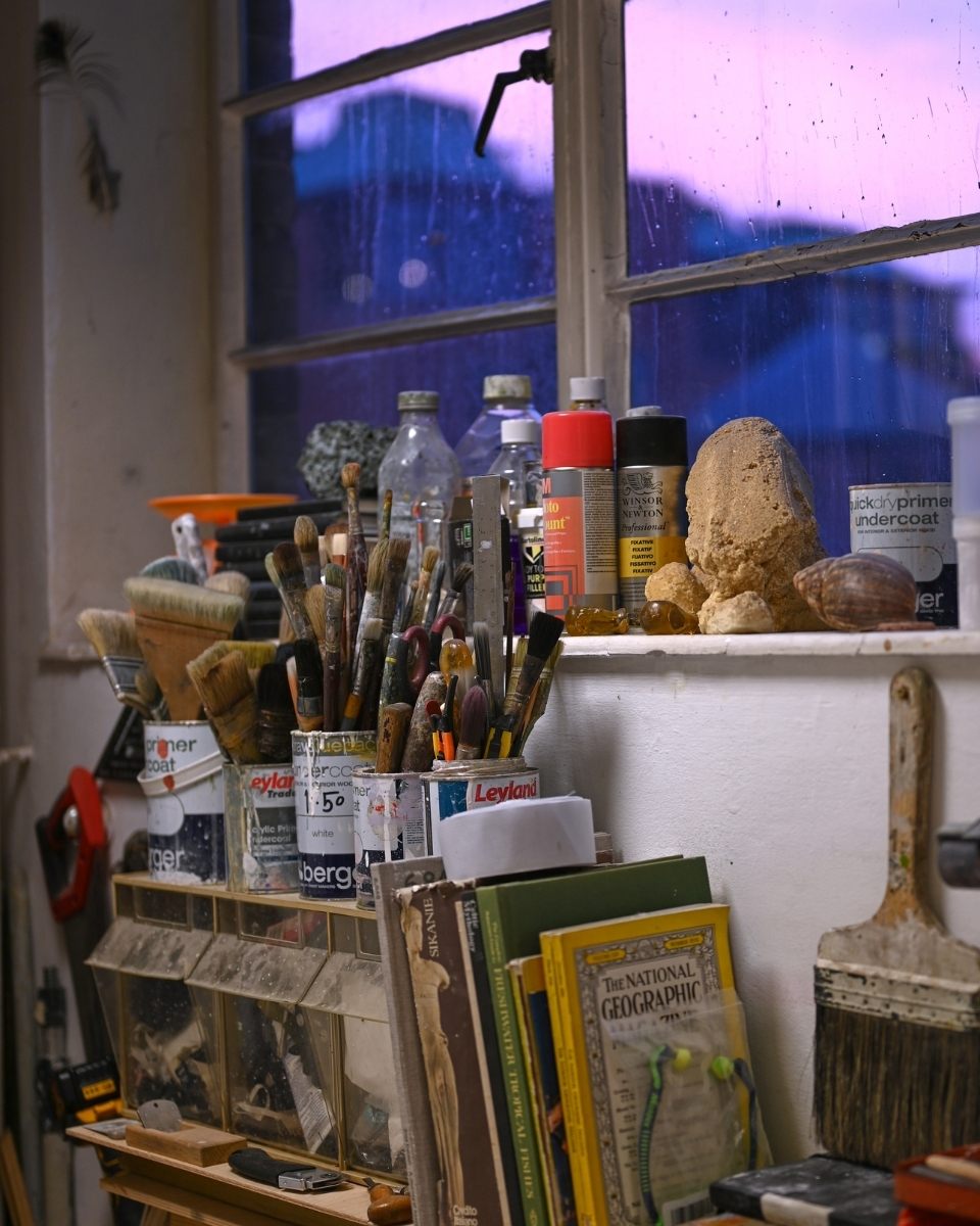 A detailed studio vignette showcasing Simon Job’s paintbrushes, industrial tools, and topographical books used for research.