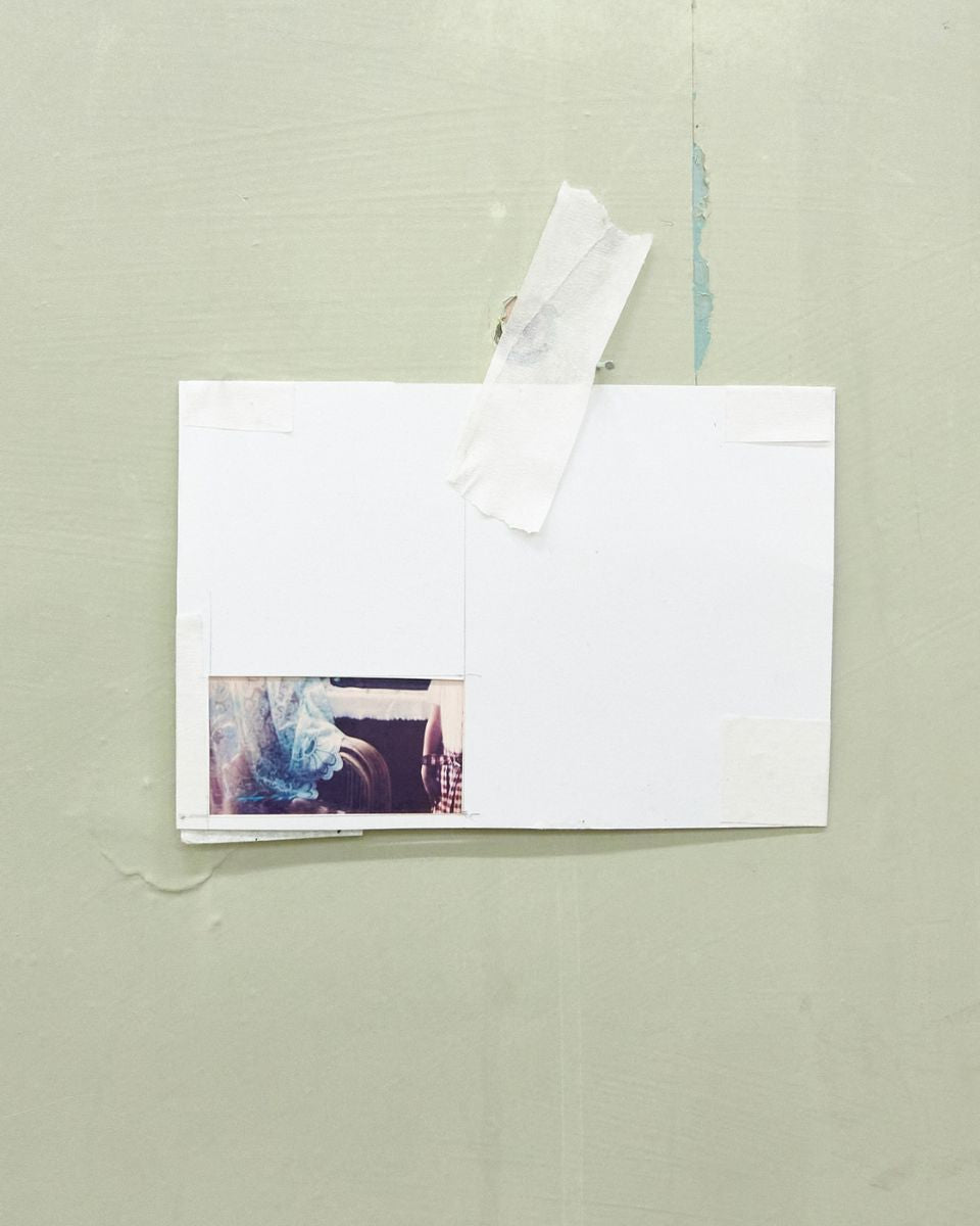 Small photographic print taped with masking tape onto a light sage green studio wall.