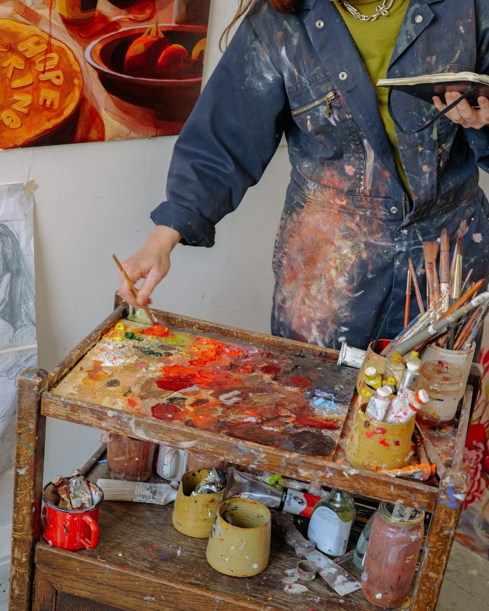 Close-up of Sophie Glover mixing a custom oil palette on a rustic wooden studio trolley.