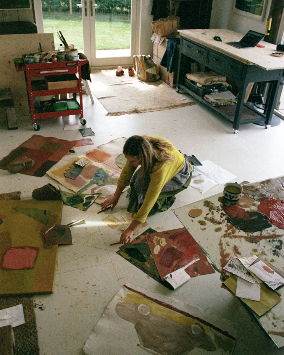 Artist Sophie Victoria Edwards crouching on her studio floor surrounded by painted paper swatches and artwork in progress.