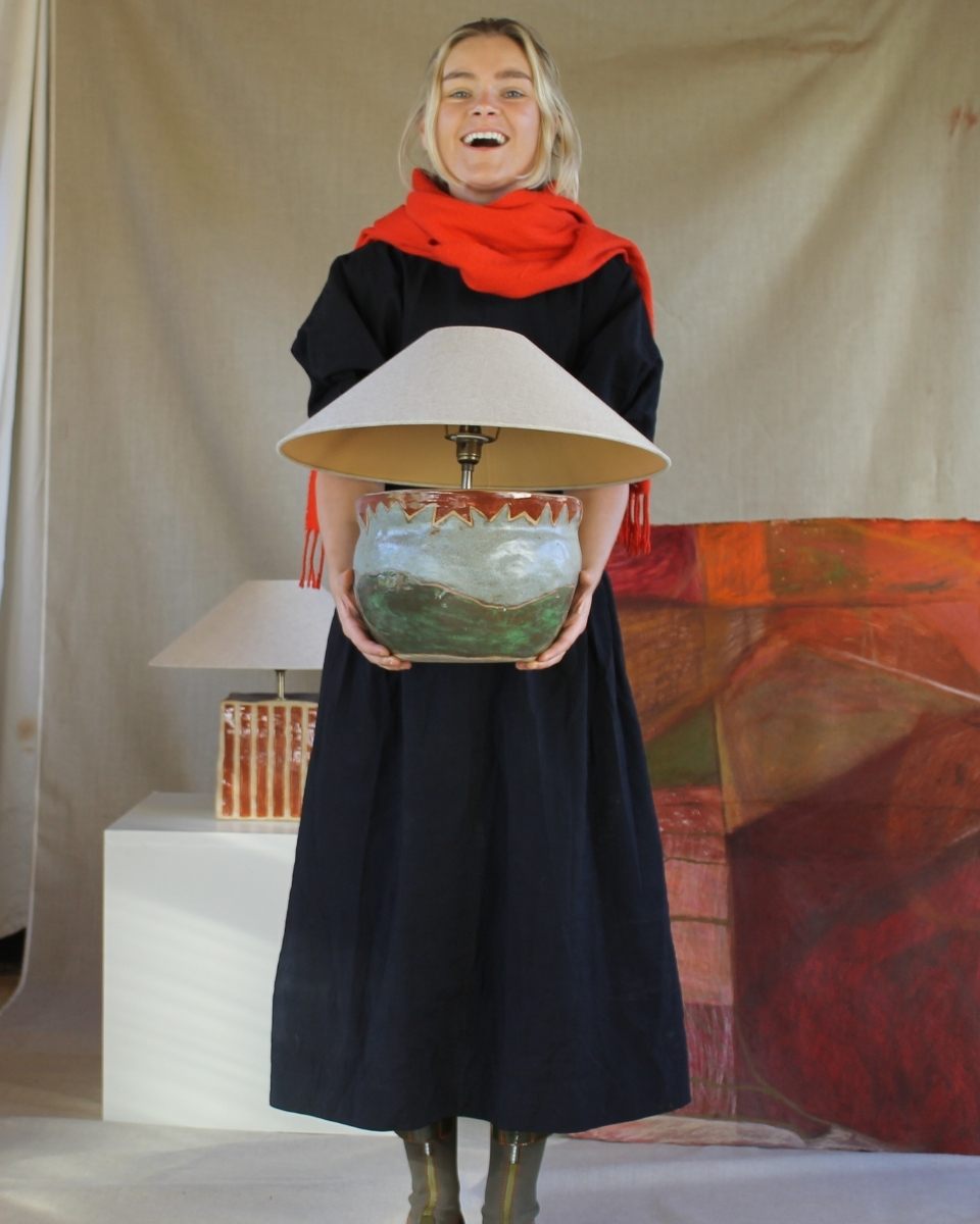 Smiling portrait of artist Sophie Victoria Edwards holding one of her unique hand-painted functional lamps.