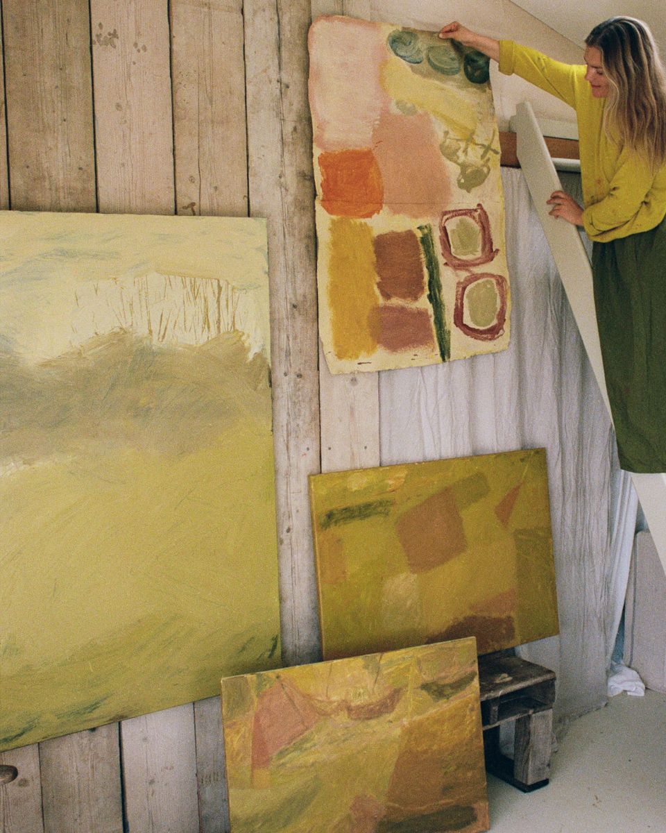 Sophie Victoria Edwards hanging an abstract earth-toned painting onto a wooden studio wall alongside other framed artwork.