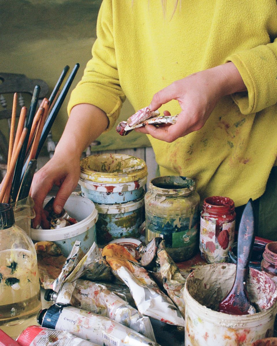 Close-up of artist Sophie Victoria Edwards sorting through paint tubes and jars on a studio supply cart.