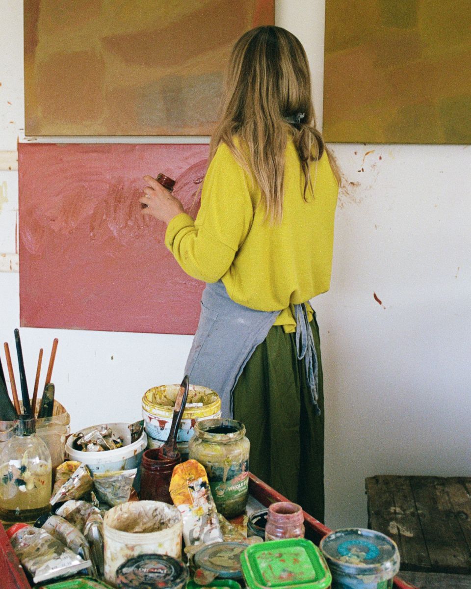 Artist Sophie Victoria Edwards viewed from behind applying paint to a canvas on her studio wall.