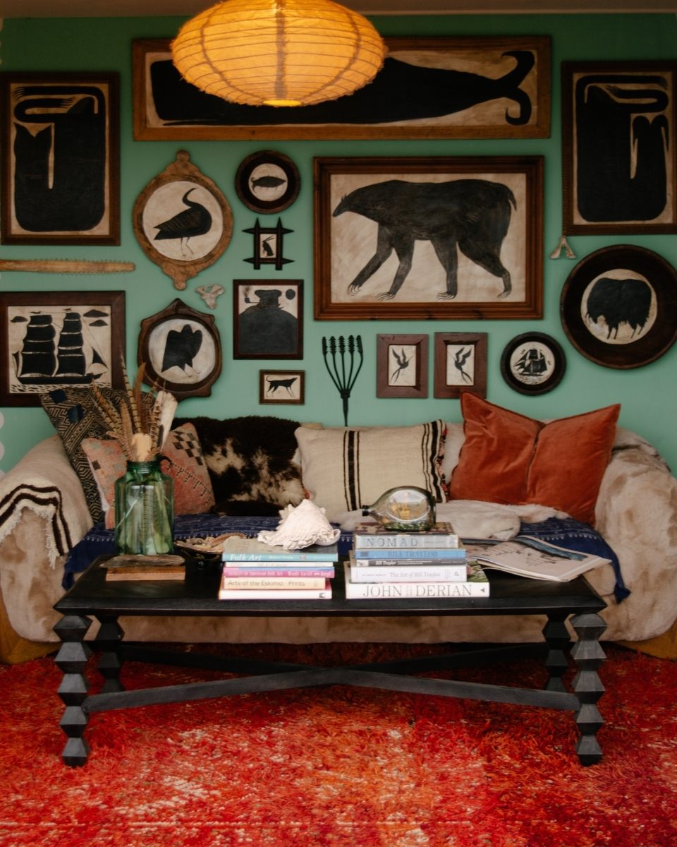 A wide-shot of Tabby Booth’s living room gallery wall, showcasing a dense, maximalist collection of her original folk-inspired artworks.
