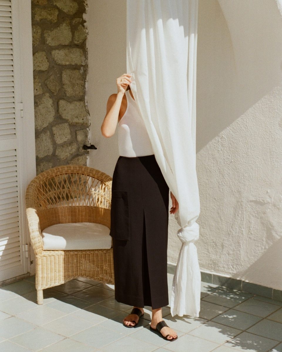 A sun-drenched self-portrait of Thea Caroline Sneve Løvstad partially hidden behind a sheer white curtain on a Mediterranean-style patio.