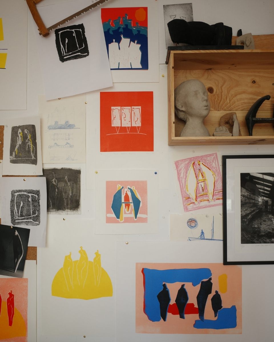 An artist studio wall filled with colourful drawings alongside an unfinished clay head sculpture.